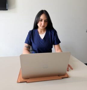 Nurse analyzing patient data on a computer while referencing a research article
