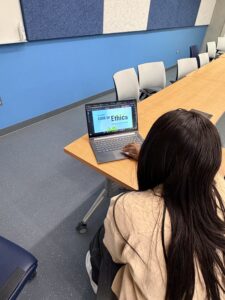 Description: Student nurse reviews CNA Code of Ethics on a laptop in a classroom.